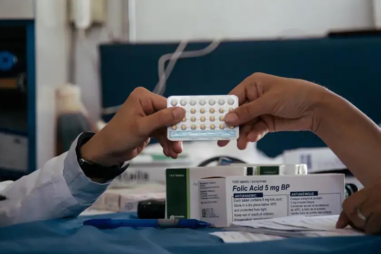 A close-up scene of two hands exchanging a blister pack of pills. 