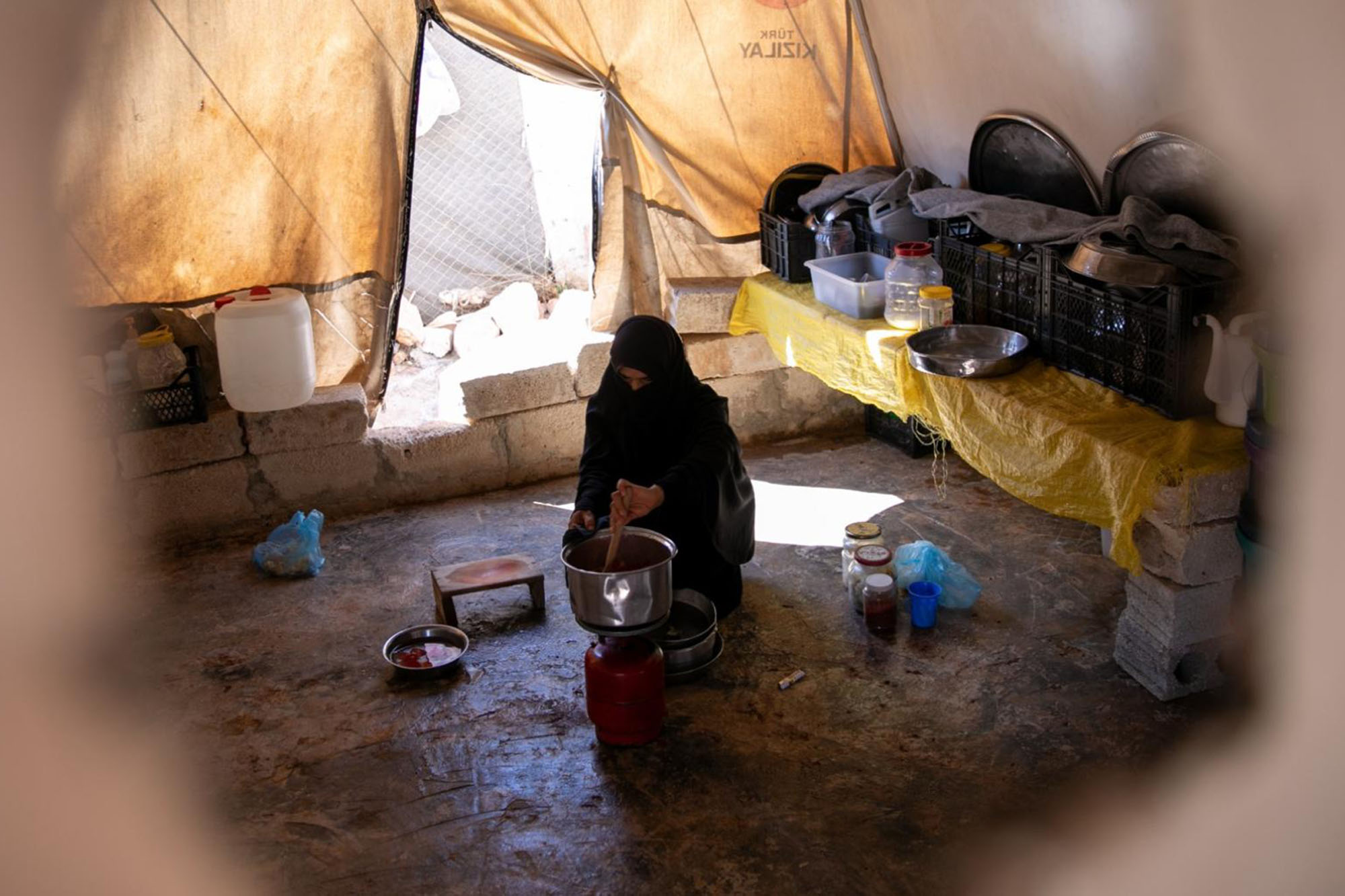 A displaced woman cooking inside a tent.