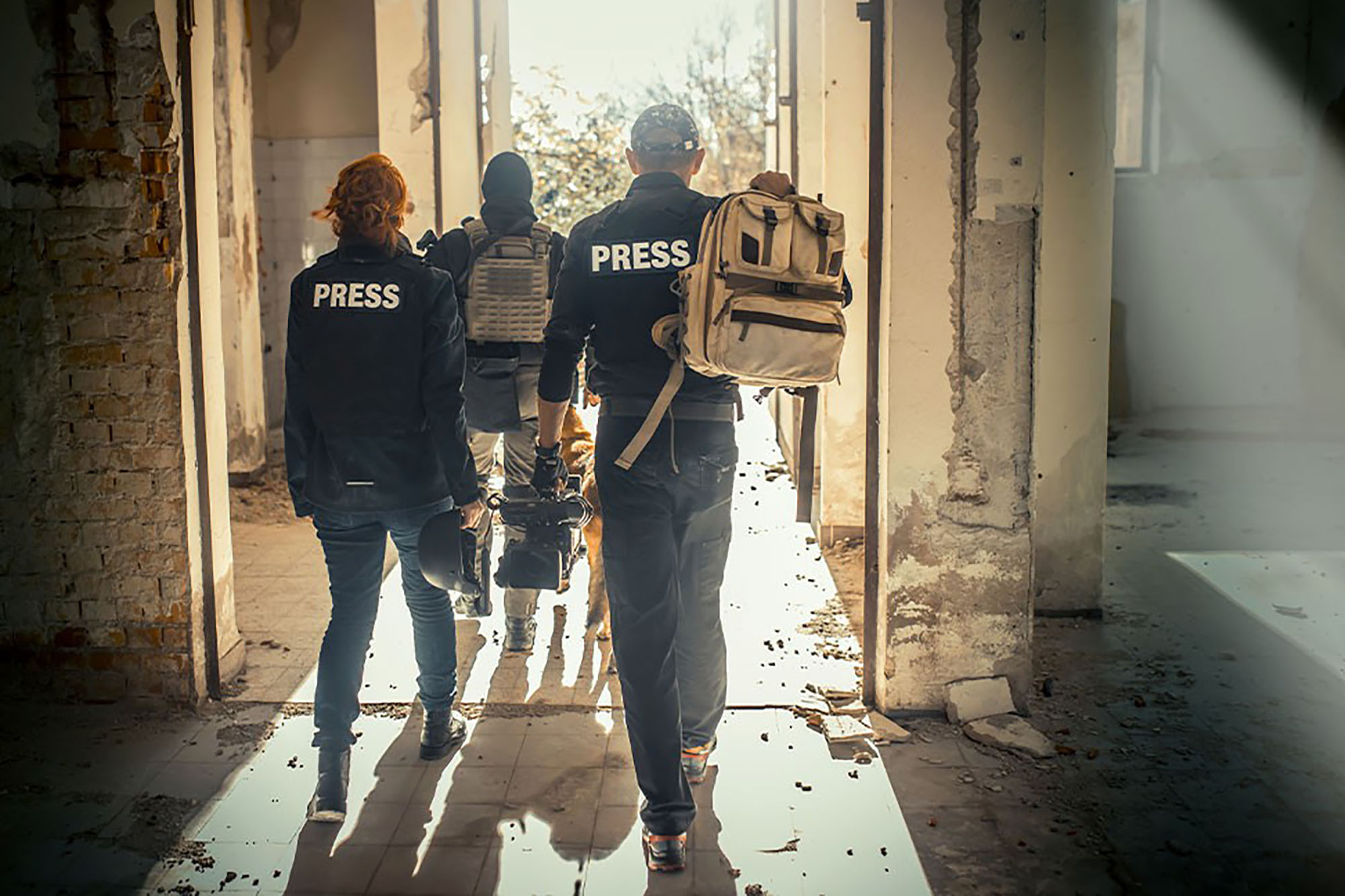 Three individuals walking through a dilapidated building with sunlight streaming in from an open doorway. 