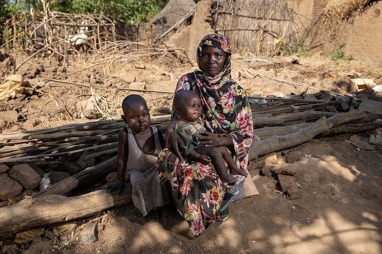A sudanese woman with her two children seated on the ground.