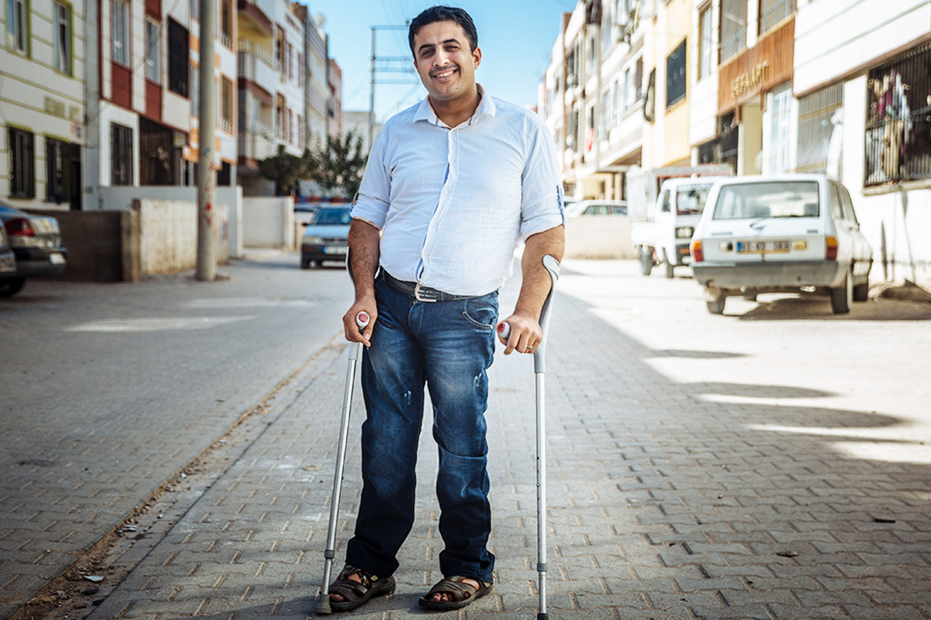 A disabled man poses for a photo in the middle of a neighborhood street.