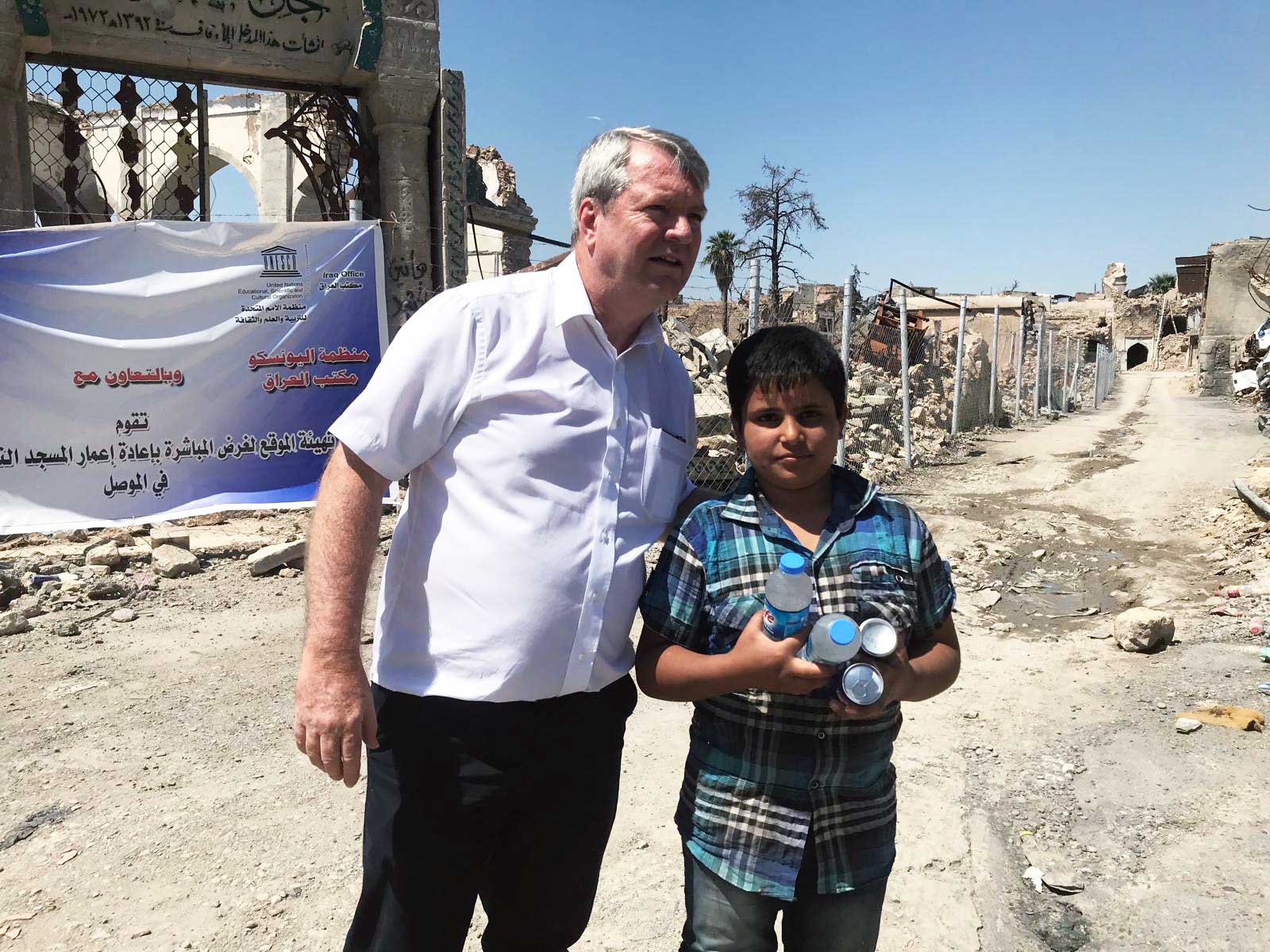 Peter stands next to a child who holds bottles of water