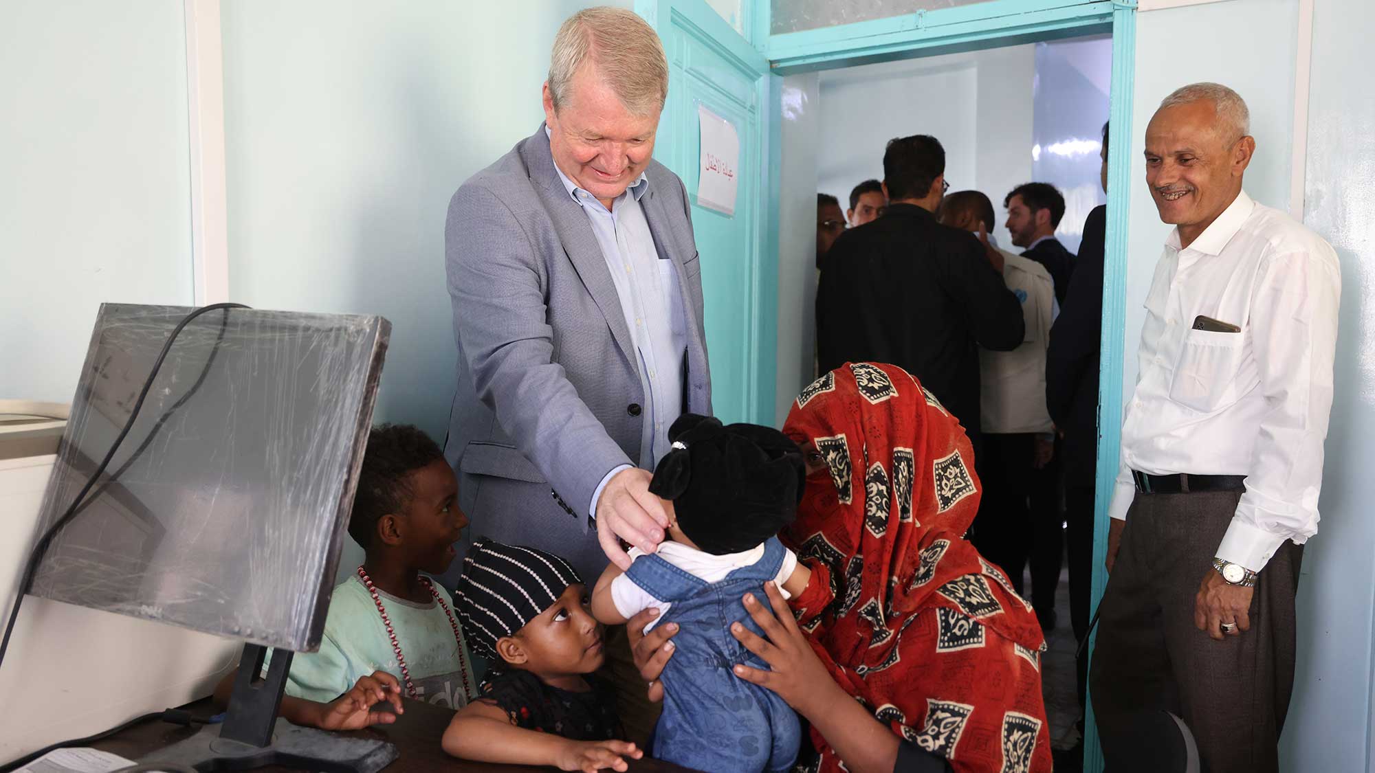Peter engages with a little child that is sitting on mother's lap inside a classroom