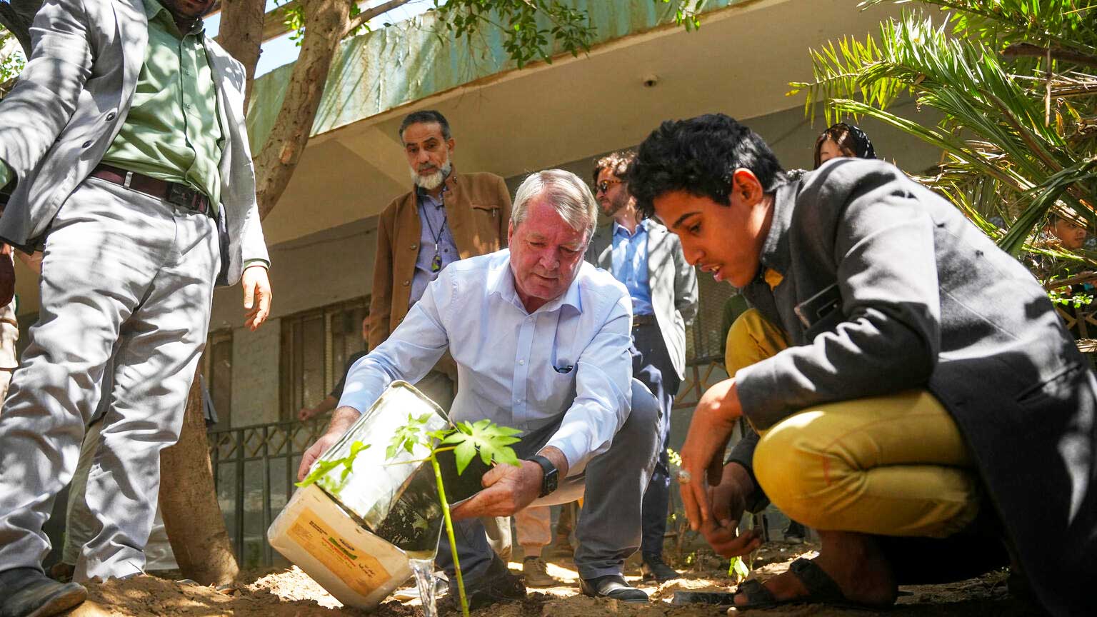 Peter watering a tree sapling with people around him