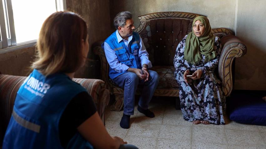 Gonzalo sits on a couch next to a woman wearing a veil who is speaking to him and to another woman