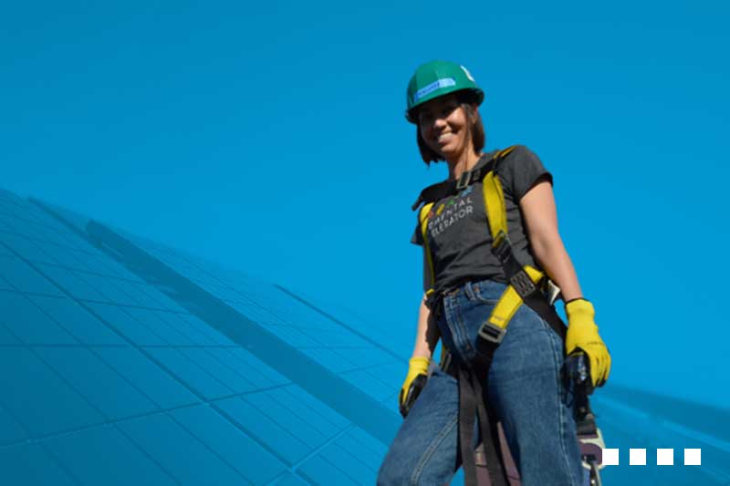 A woman worker in a harness next to solar panels