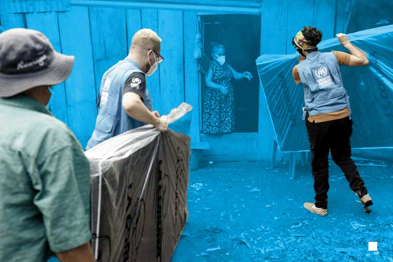 two UNHCR employees deliver mattresses to an elderly woman