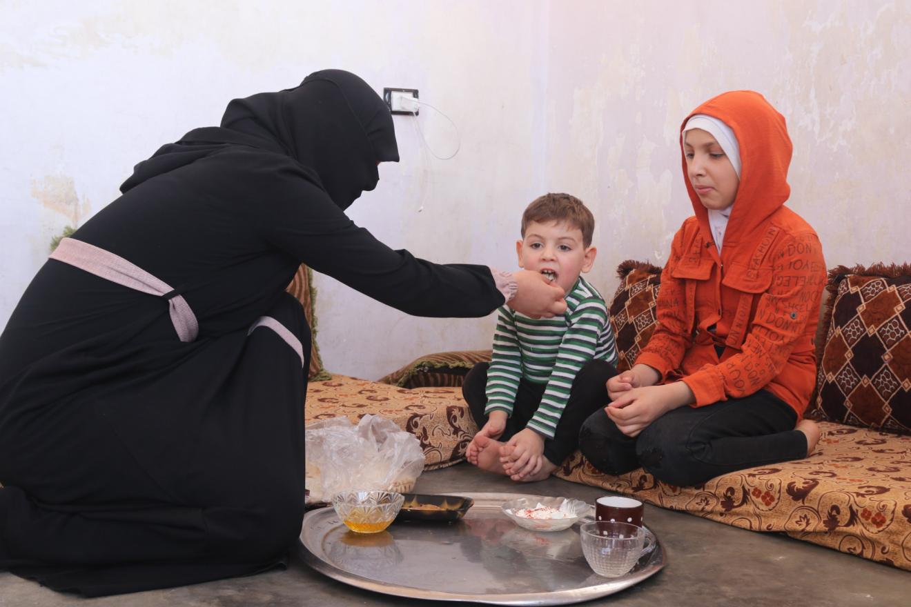 A mother feeding her son with her daughter watching.