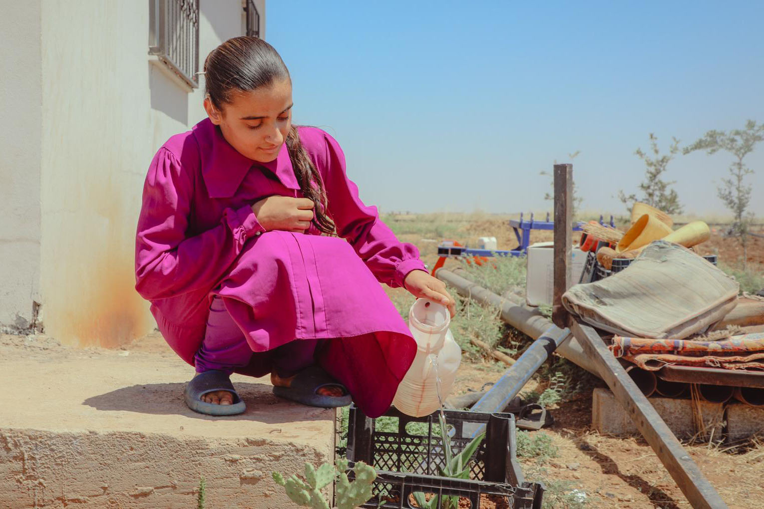 A young lady watering a plant outside.