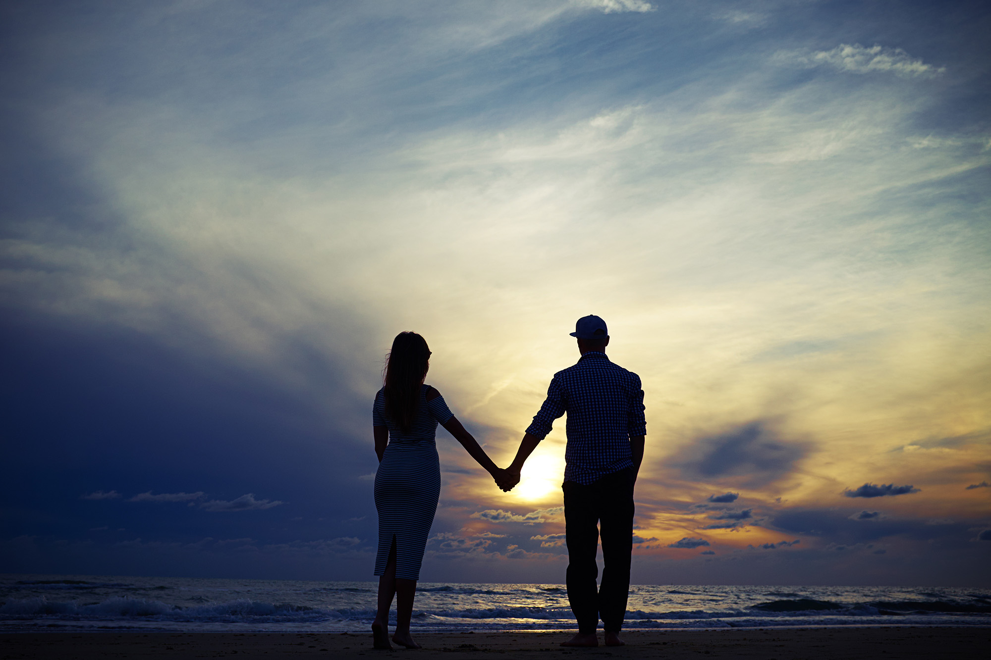 Romantic couple holding hands while looking to the sunset.